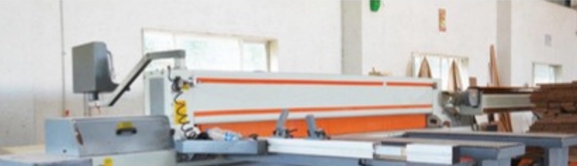 A sliding-table panel saw on the Wada factory floor, with timber stock stacked alongside.